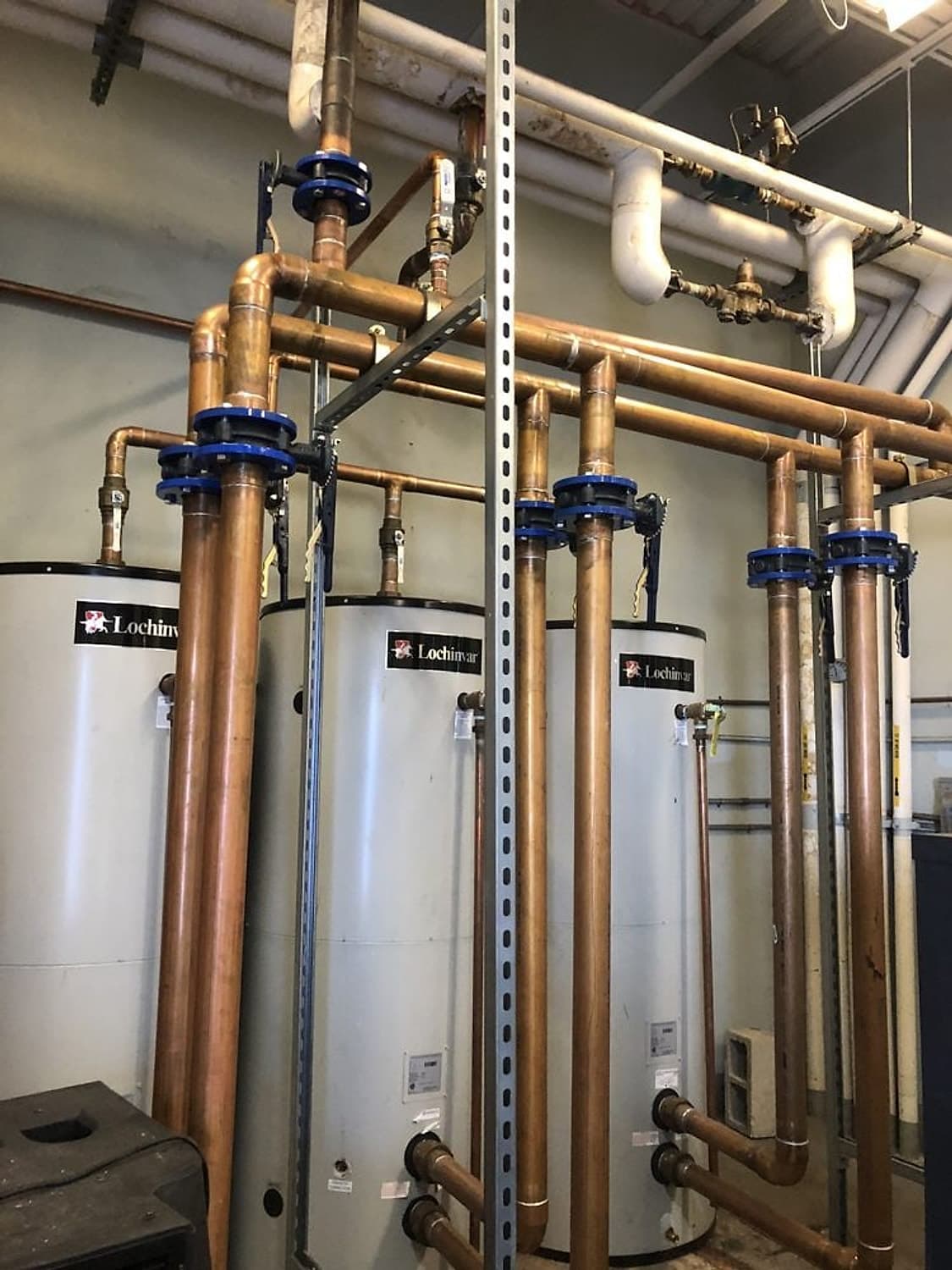 Three Lochinvar commercial water heaters connected by copper piping and blue valves in a utility room