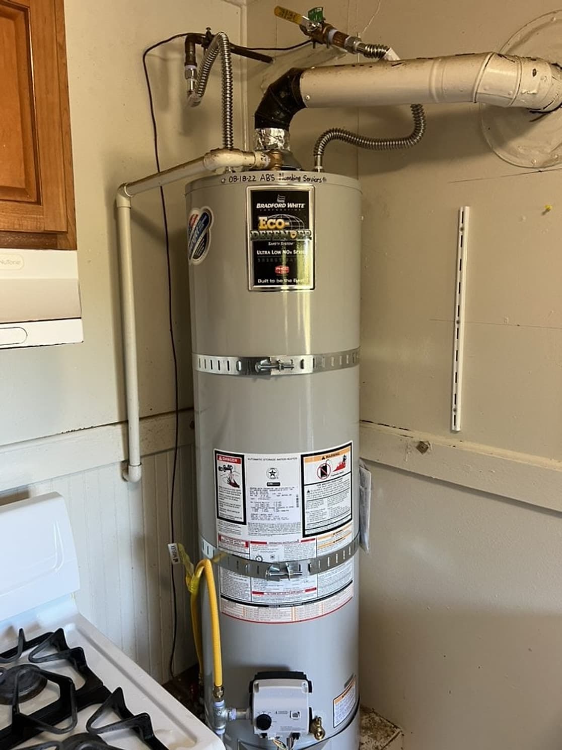 New Bradford White gas water heater with seismic straps, new vent pipe and gas connector in a kitchen closet