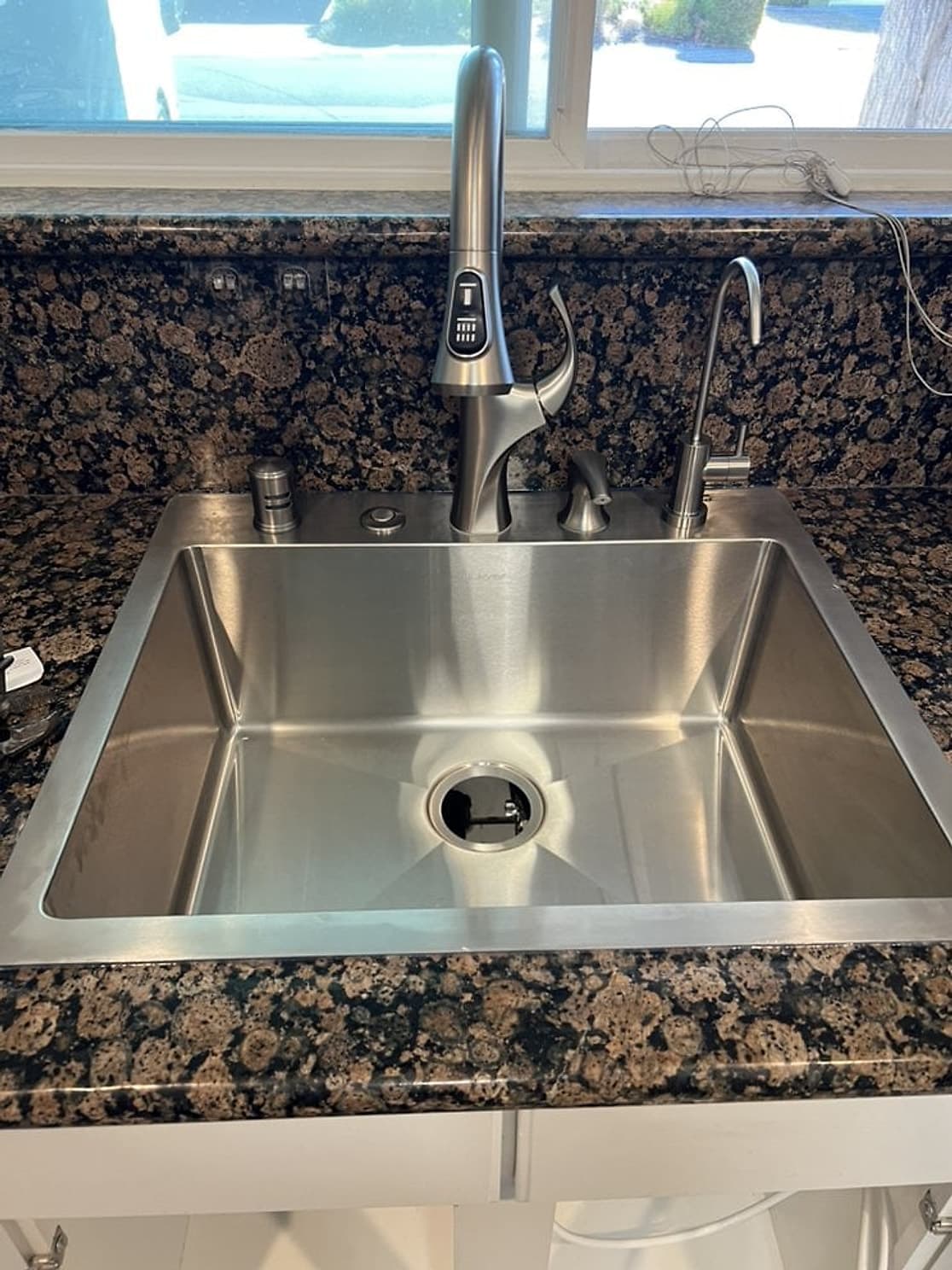 New stainless steel kitchen sink with a pull-down faucet and a separate filtered-water tap in a granite counter