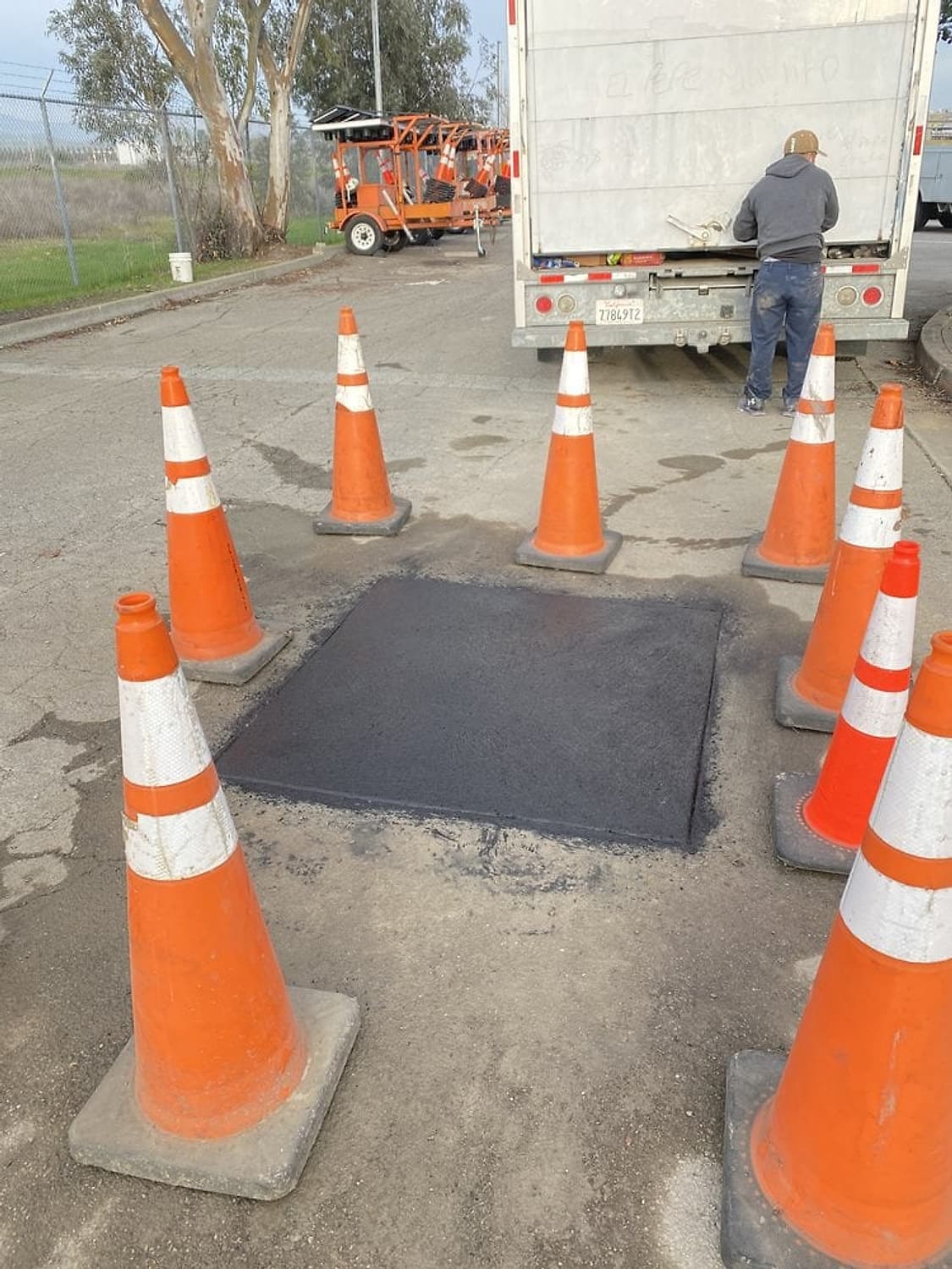 Fresh asphalt patch in the street surrounded by orange traffic cones after a sewer lateral connection, work truck behind
